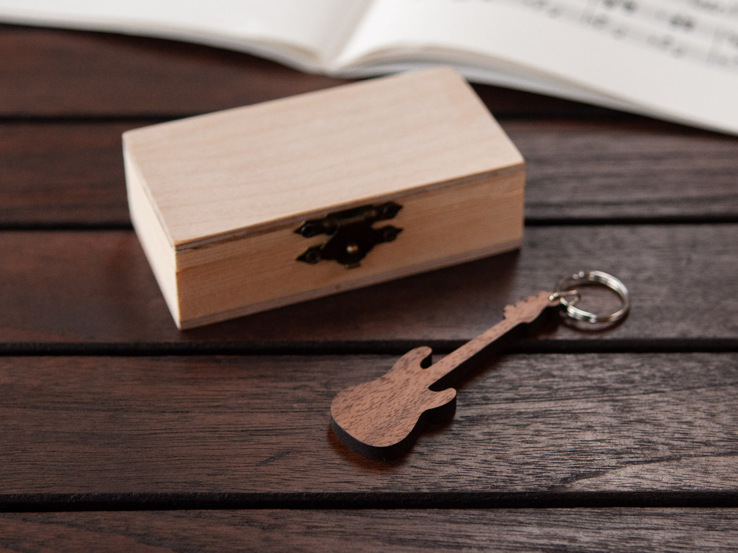 A keychain in the shape of a bass guitar made from walnut, in front of a small wooden box