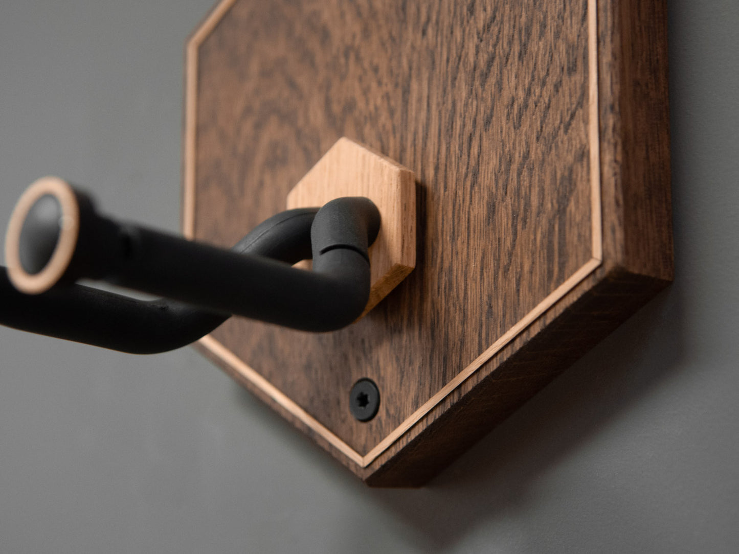 Details of a guitar wall mount in the shape of a hexagon. The body is made from darkened oak wood, with contrasting light oak strips