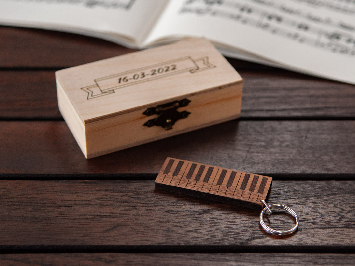 A keychain shaped like a piano in front of a small engraved wooden box.