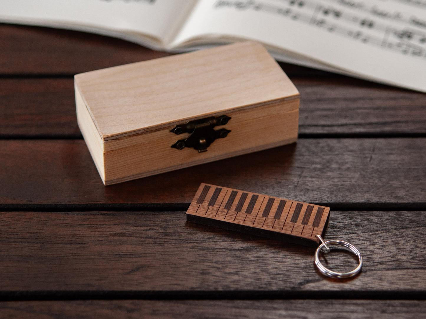 A piano keychain positioned in front of a small wooden box.