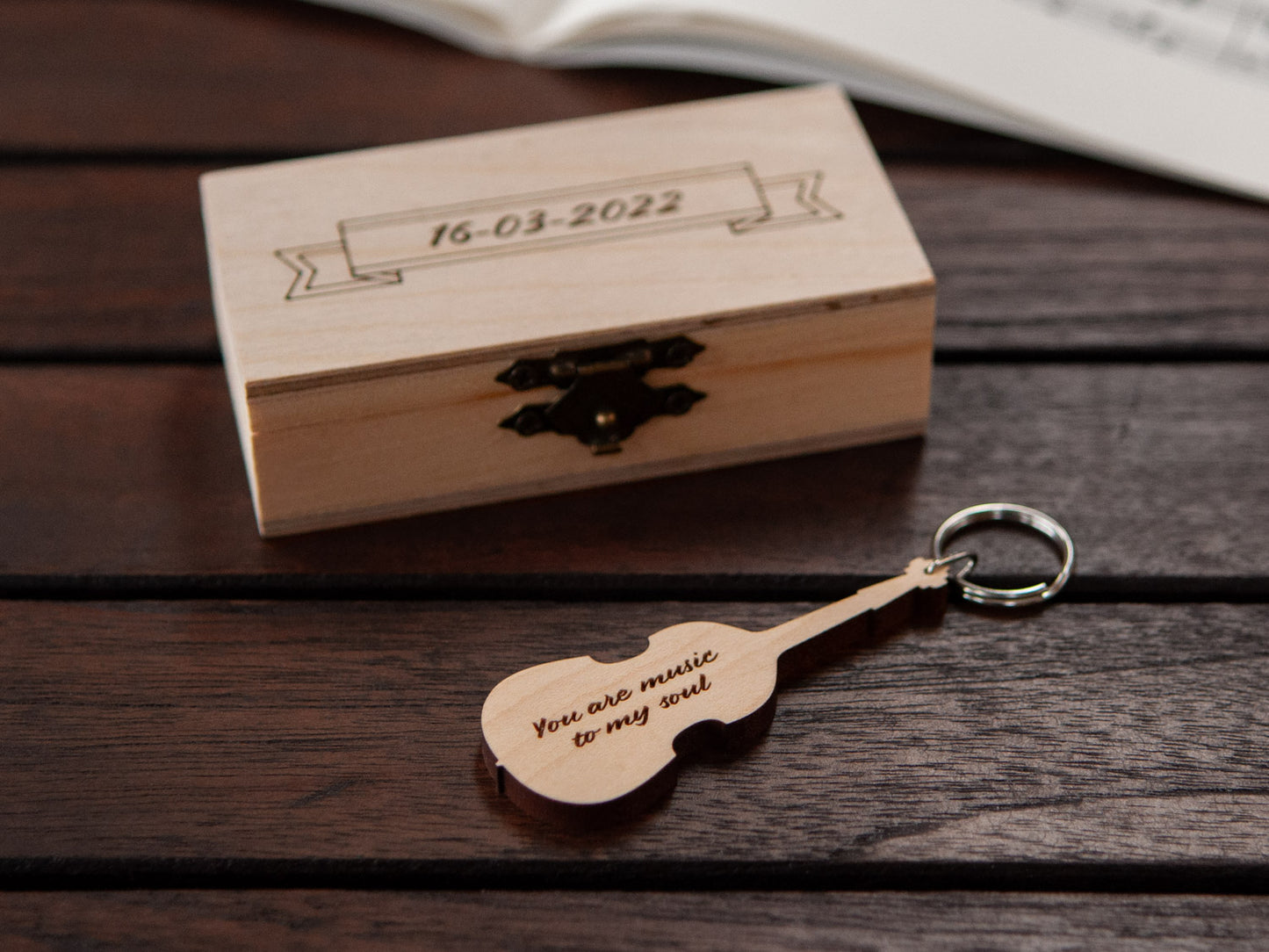 A keychain in the shape of a double bass in front of a small wooden box, with custom engraving.
