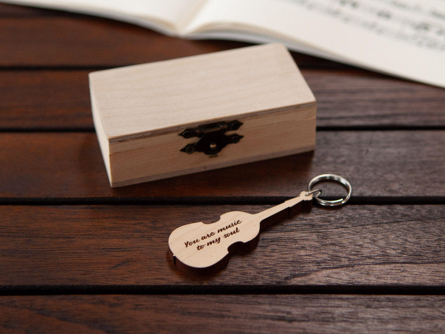 A keychain in the shape of a double bass in front of a small wooden box, with custom engraving.