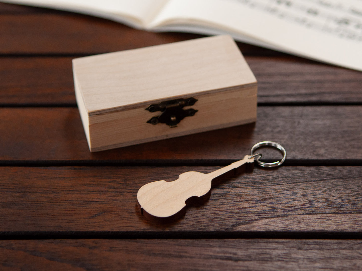 A keychain in the shape of a double bass made from maple, in front of a small wooden box