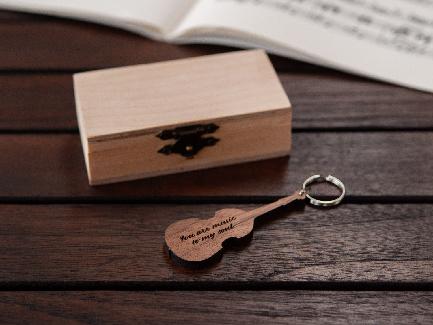 A keychain in the shape of a double bass in front of a small wooden box, with custom engraving.