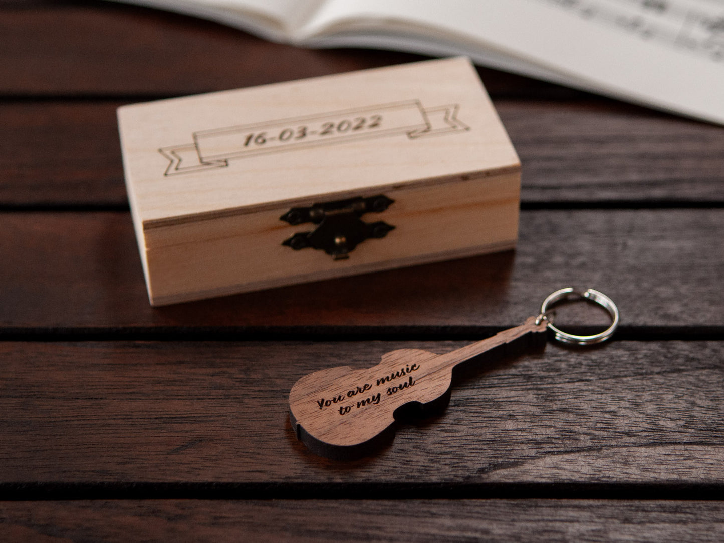 A keychain in the shape of a double bass in front of a small wooden box, with custom engraving.
