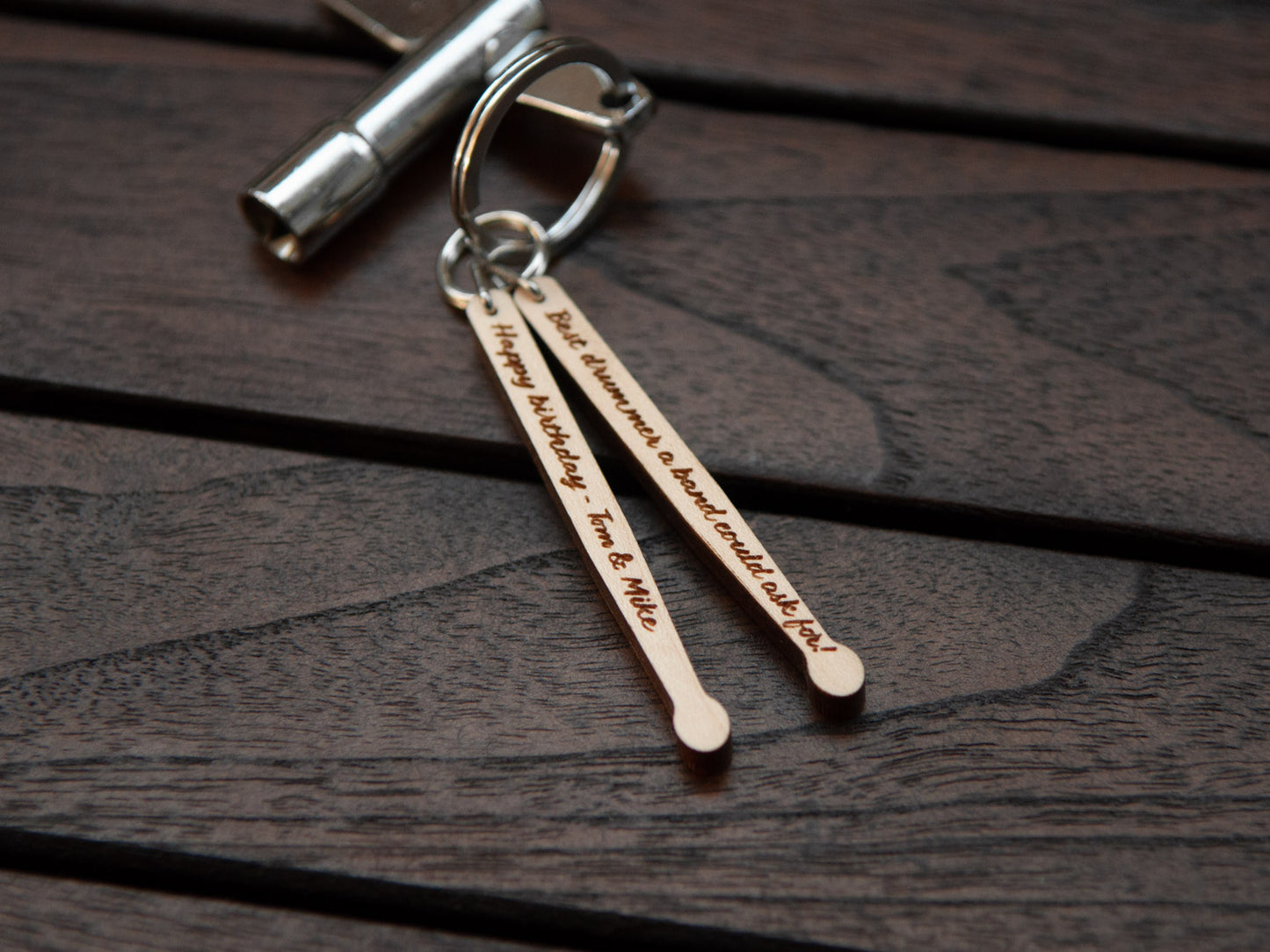 Details of a keychain in the shape of drumsticks with engraving, made from maple wood. A drum key is also attached to the key ring.