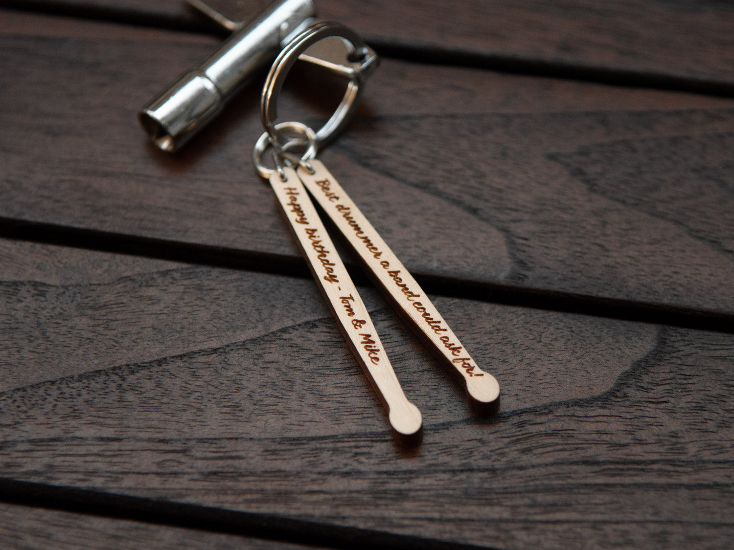 Details of a keychain in the shape of drumsticks with engraving, made from maple wood. A drum key is also attached to the key ring.