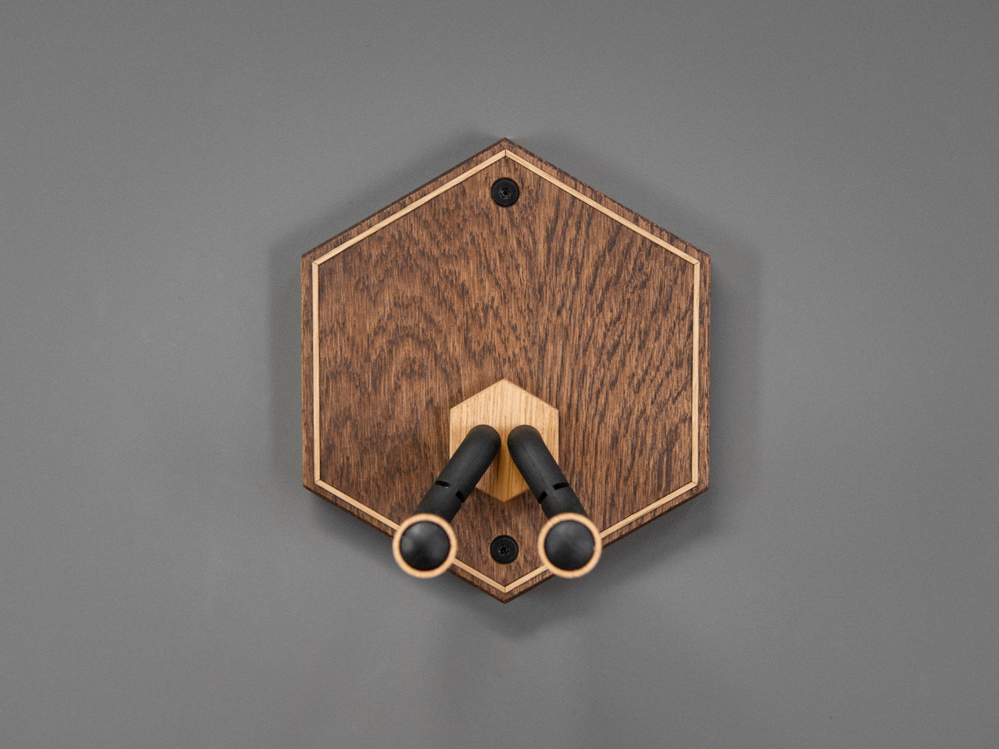 Guitar wall mount in the shape of a hexagon. The body is made from darkened oak wood, with contrasting light oak strips